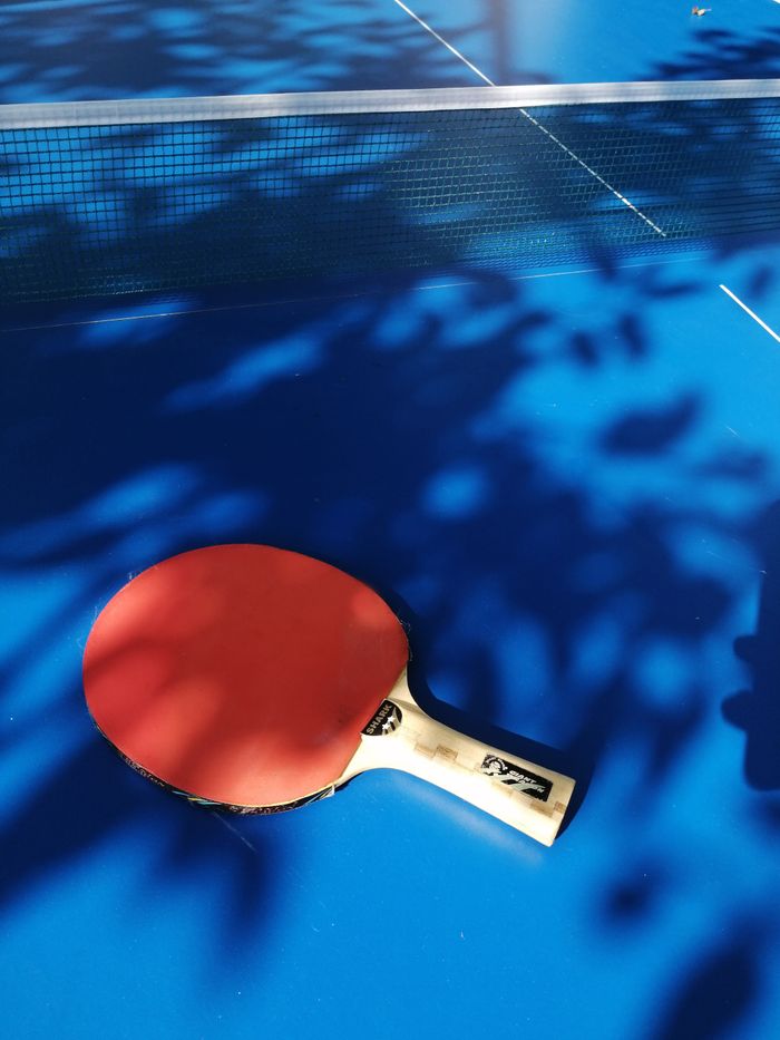 A red table tennis racket on a blue table with shadow patterns in Obninsk, Russia.